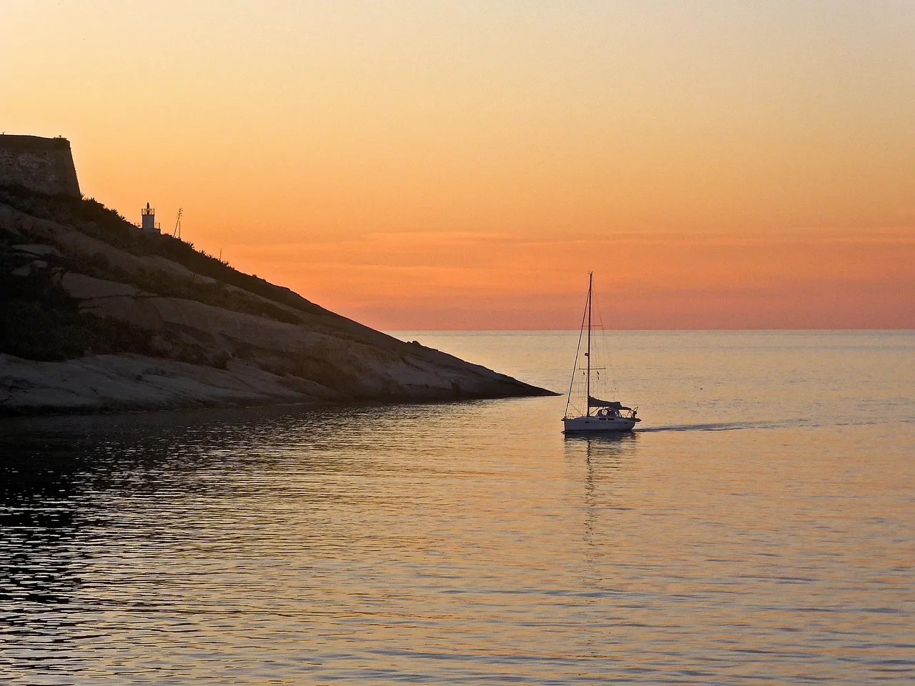 Voilier glissant sur la mer au coucher du soleil, au pied d'un cap de Corse