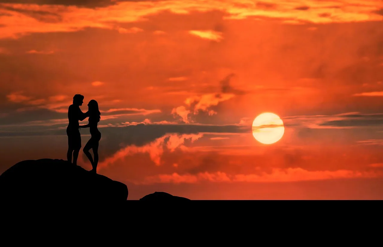 Silhouettes d'un couple sur un rocher face au coucher du soleil