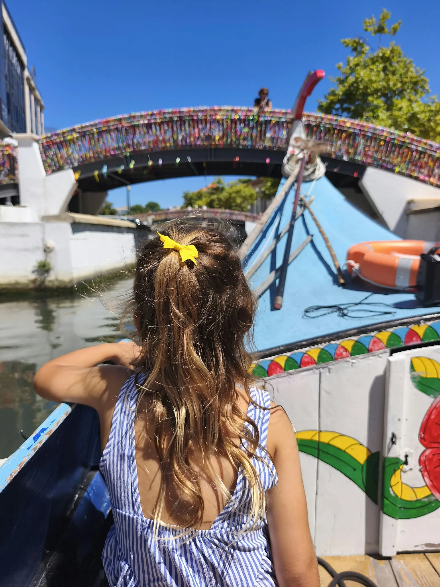 Enfant à bord d'un moliceiro coloré passant sous un pont d'Aveiro