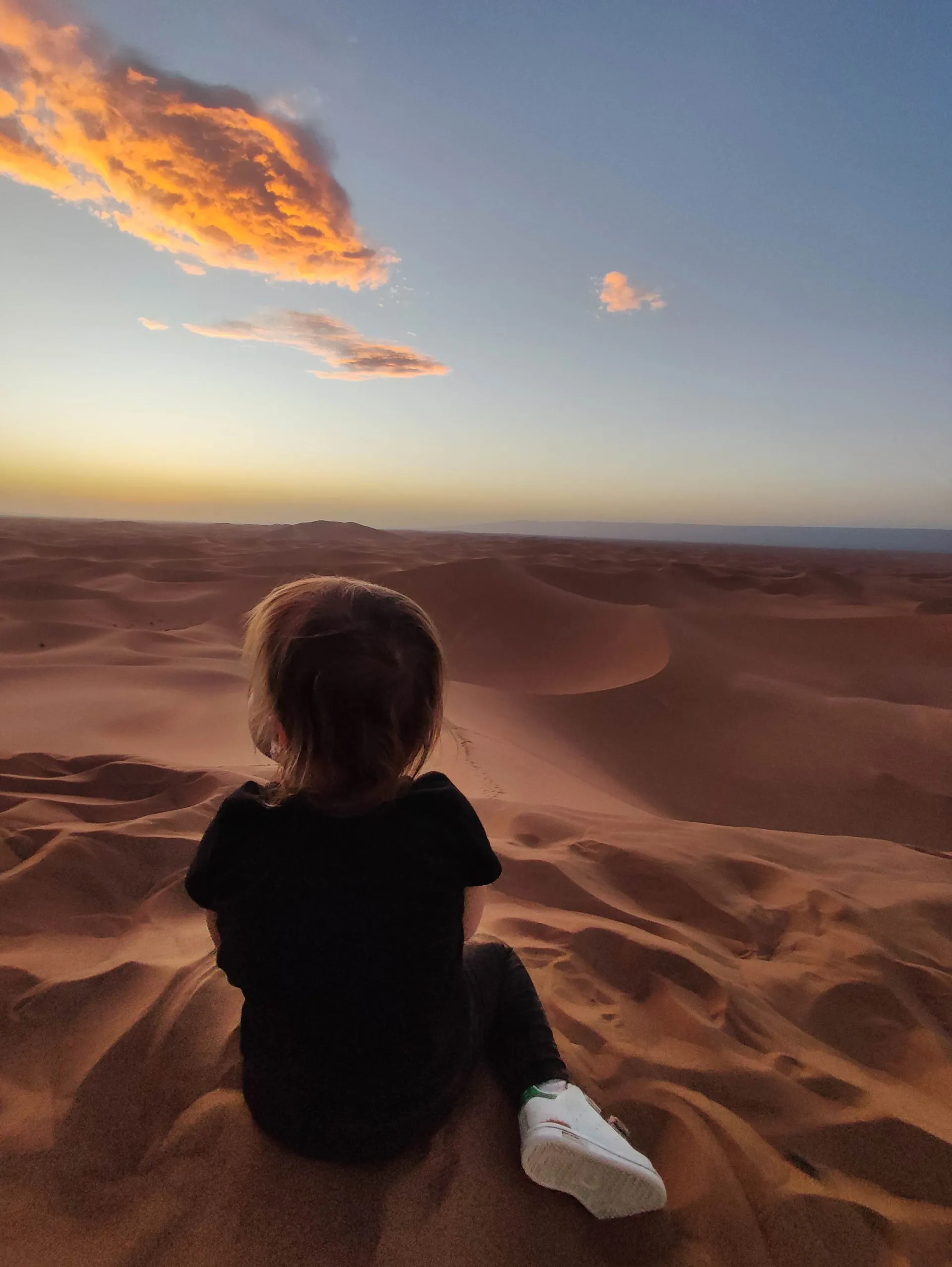 Enfant assis au sommet d'une dune de l'Erg Chebbi au coucher du soleil