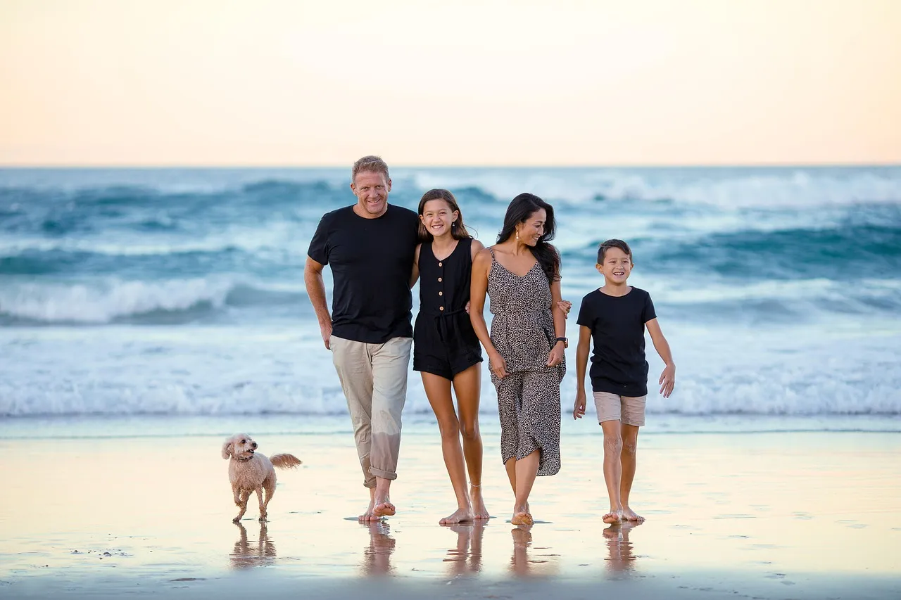 Famille marchant au bord de l'eau sur une plage, avec son chien