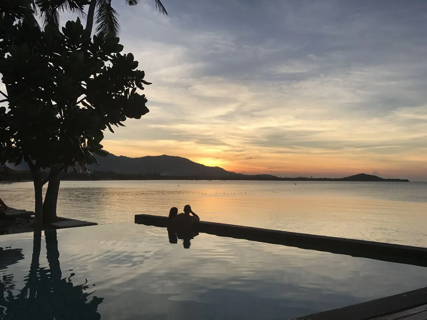 Couple dans une piscine à débordement face au coucher de soleil sur la mer